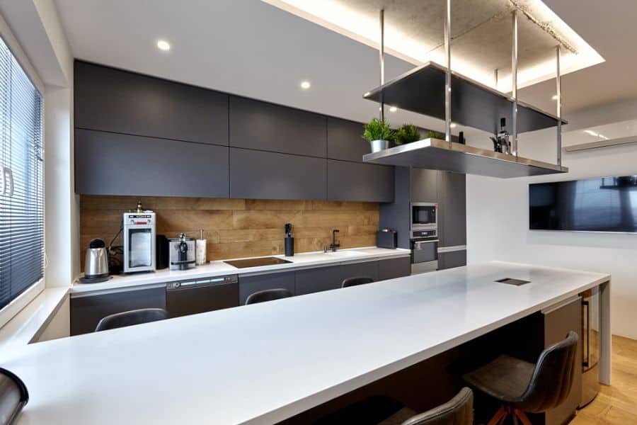 Modern industrial kitchen with dark cabinets, wood backsplash, white island, and hanging shelves.