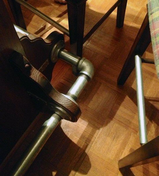 Industrial-style brass pipe foot rail attached to a wooden bar on parquet flooring.