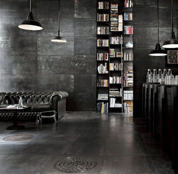 Industrial man cave with black leather sofa, floor-to-ceiling bookshelf, and hanging pendant lights