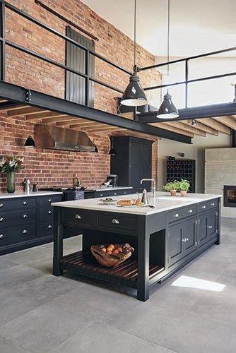 Industrial kitchen with exposed brick walls, black cabinets, and a large island countertop.