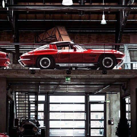 An industrial-style garage featuring a classic red Corvette displayed on a mezzanine level.