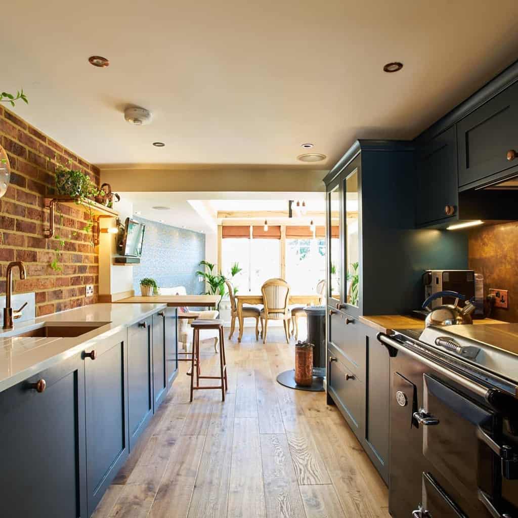 industrial galley kitchen wood flooring black cabinets brick wall dining table