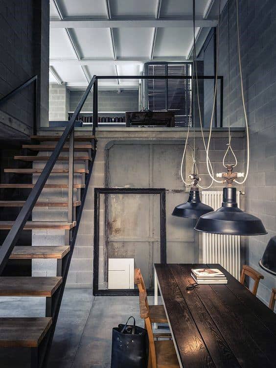 Industrial-style space with concrete walls, wooden staircase, and black pendant lighting.