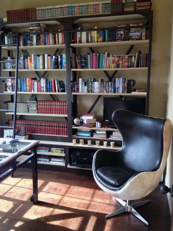 A cozy library with a leather swivel chair, a book-filled bookshelf, and a glass desk bathed in sunlight