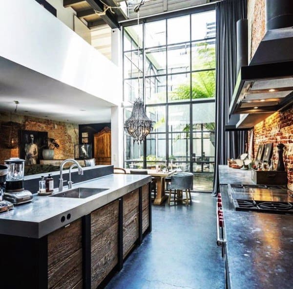 Industrial kitchen with exposed brick walls, large windows, and a central chandelier.