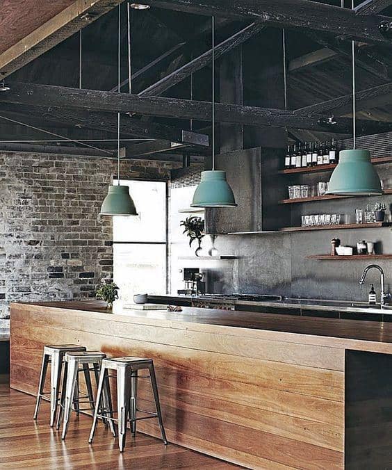 Industrial kitchen with exposed brick walls, wooden counters, and green pendant lights.