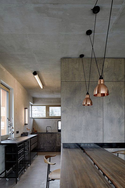 Industrial kitchen with concrete walls, wooden table, and copper pendant lights.