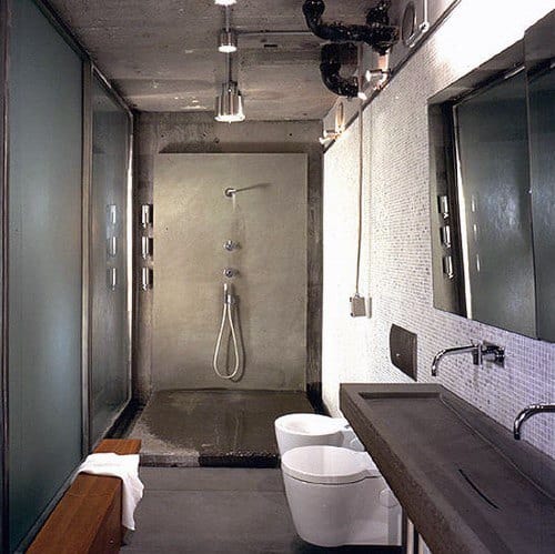 Industrial bathroom with concrete shower, sleek fixtures, and frosted glass panels.