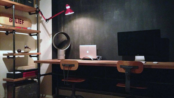Minimalist workspace with two wooden chairs, a laptop, desktop monitor, and shelves on a dark wall background