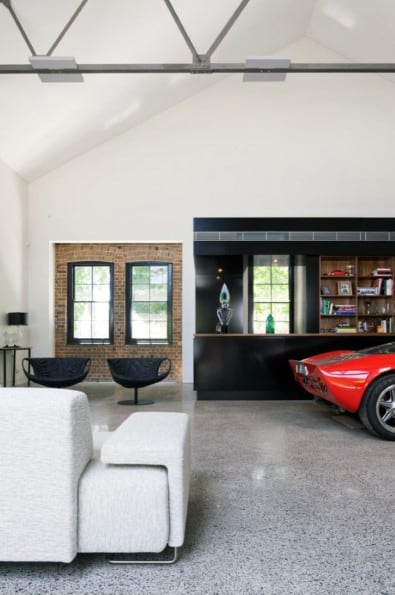 Modern loft with a sleek black bookshelf, red sports car in the garage, white sofa, and two chairs near large windows