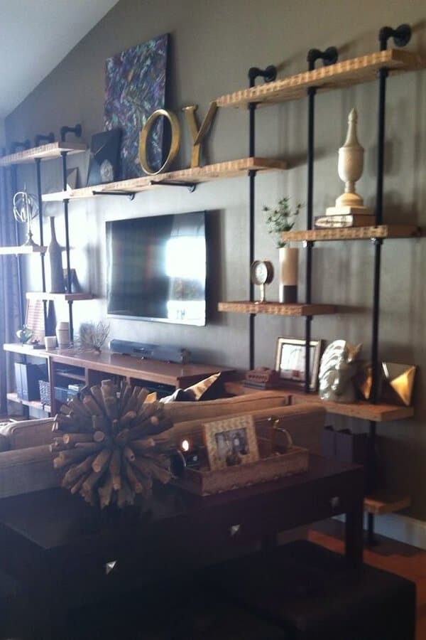 Industrial-style living room with metal-framed wooden shelves, wall-mounted TV, and rustic decor.