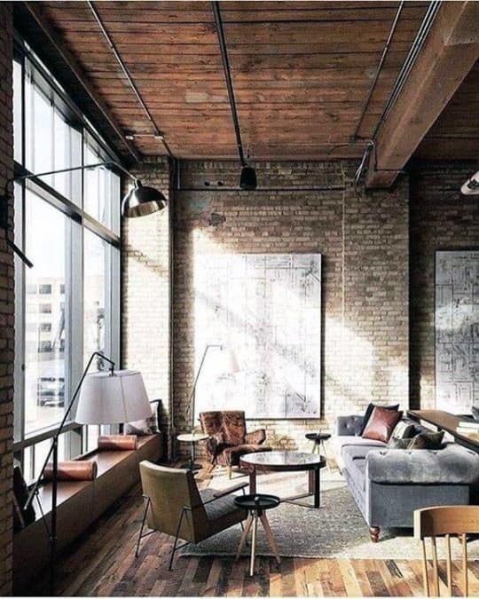 Industrial-style living room with brick walls, wooden ceiling, and large windows.