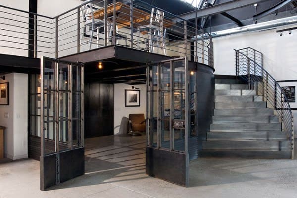 Industrial loft with steel staircase, glass doors, and open mezzanine.