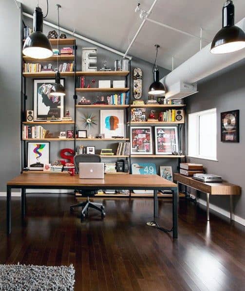 Modern home office with a wooden desk, bookshelves filled with books, art, and decor against a gray wall