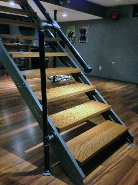 Industrial-style floating stairs with metal piping and wooden steps in a modern basement.