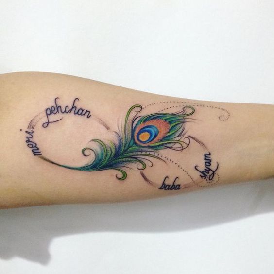 Elegant peacock feather tattoo on the forearm with vibrant green, blue, and gold hues, featuring delicate script reading 'meri pehchan baba Islam' in a flowing design.