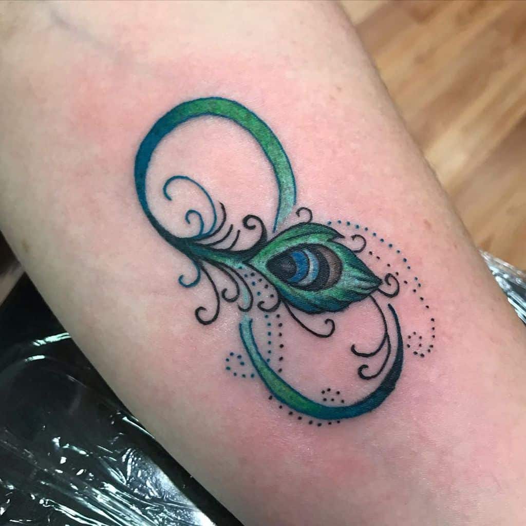 Elegant peacock feather infinity tattoo with vibrant blue and green hues, delicate swirls, and fine dot detailing on the skin.