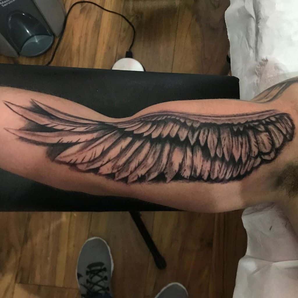 Bold tattoo of a single angel wing, with detailed feathering and dynamic shading, creating a dramatic and elegant look