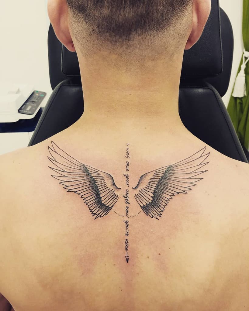 Minimalist angel wings tattoo with a delicate script reading, 'I was once your angel, now you're mine,' and an arrow below.