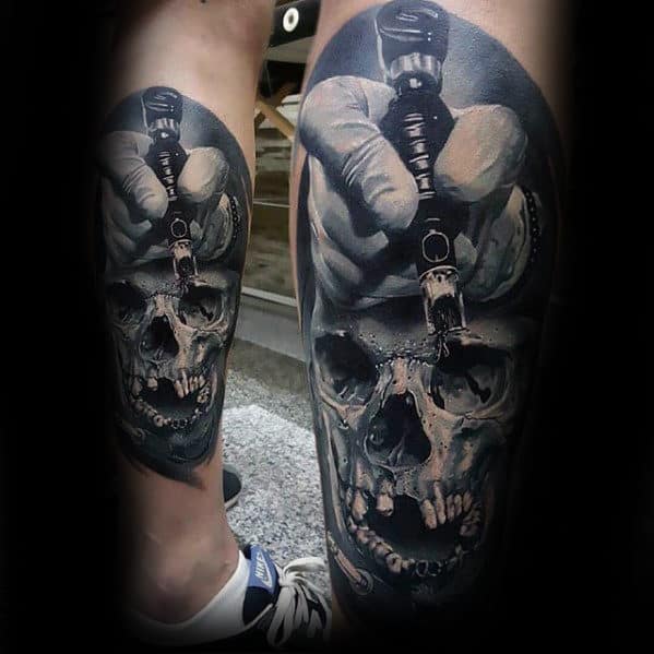 Tattoo of a skull with a hand holding a tattoo machine above it on a person's leg