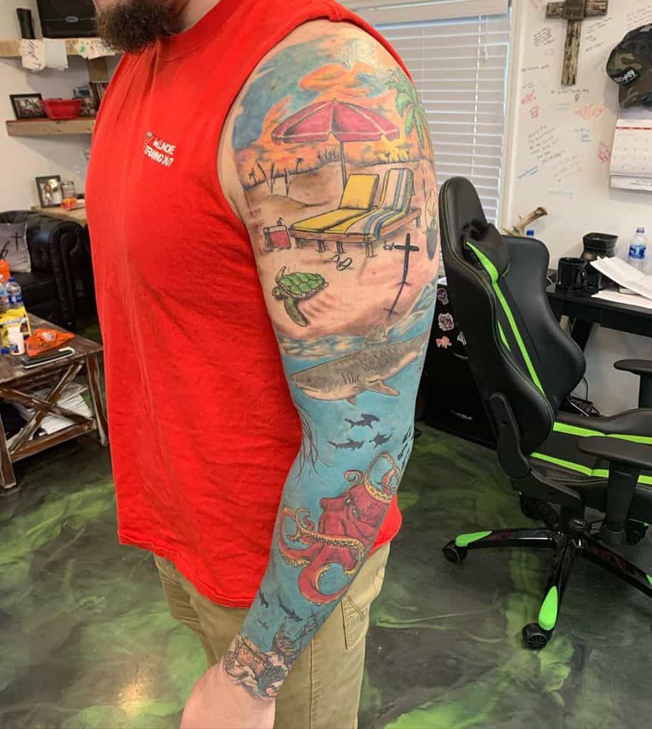 Vibrant tattoo with a beach scene, featuring lounge chairs, an umbrella, and a turtle, transitioning into an ocean theme with a shark, swimming fish, and a red octopus