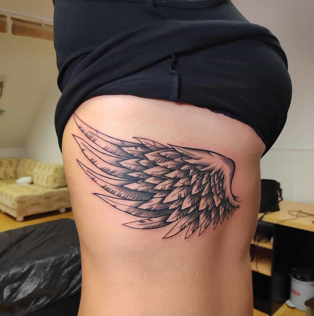 Side tattoo of an angel wing, featuring detailed feathers and bold black ink