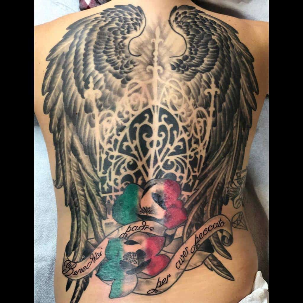 Intricate tattoo featuring angel wings, gothic filigree, Italian script, and red, green, and black floral accents