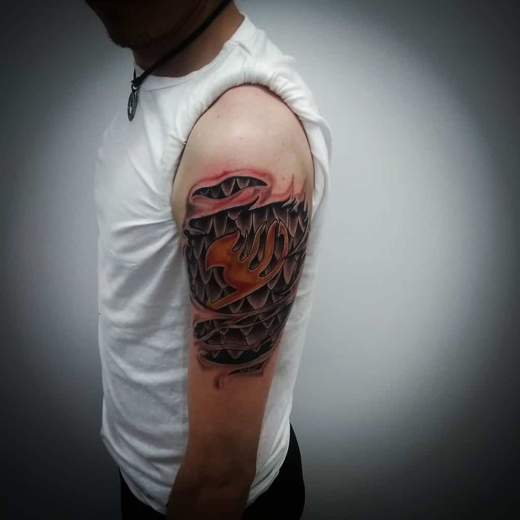 Realistic 3D Fairy Tail guild emblem tattoo on the upper arm, designed to look like it's emerging from beneath torn skin with dark shading.