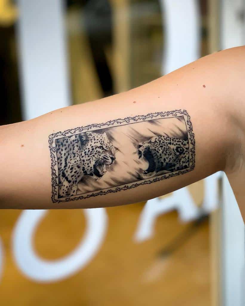 A captivating tattoo of two jaguars facing off in a frame-like design, featuring detailed realism and shading, placed on the upper arm.