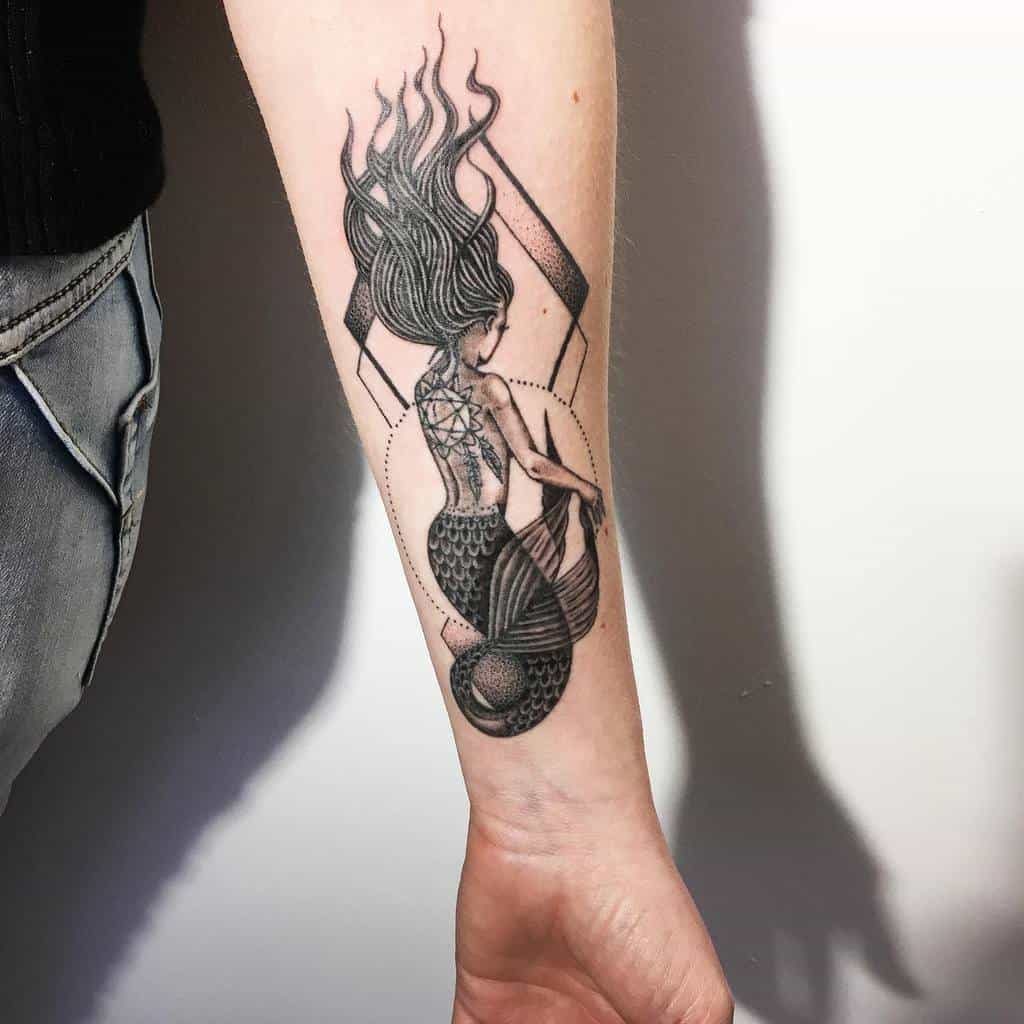 Black and grey tattoo of a mermaid with flowing hair, suspended by ropes in a geometric frame, with intricate shading and details.