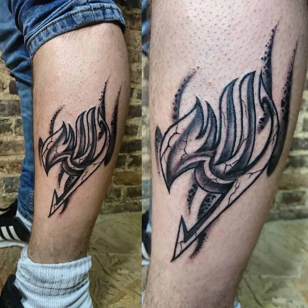 Black and grey Fairy Tail guild emblem tattoo on the calf, featuring sharp shading and a torn-skin effect for a bold and dynamic look.