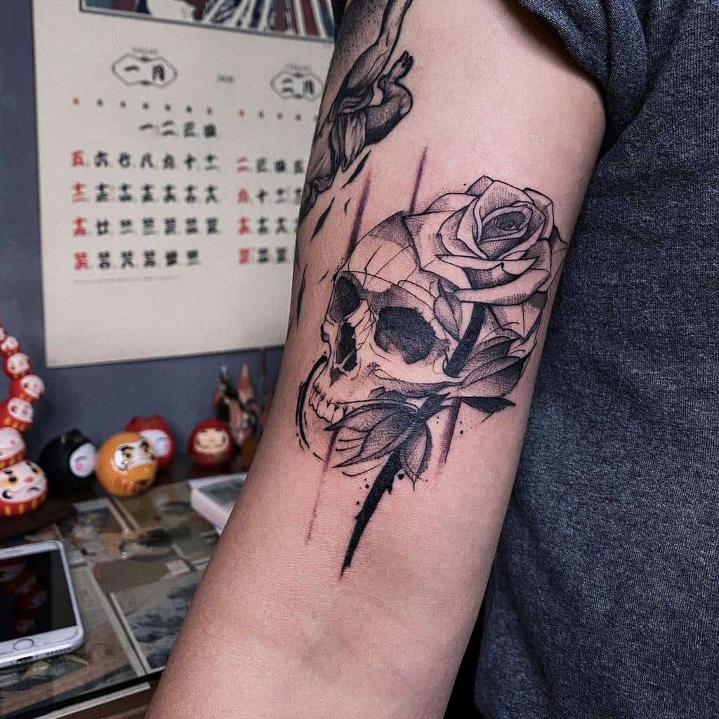 Black and white tattoo of a skull entwined with a vibrant rose on an arm