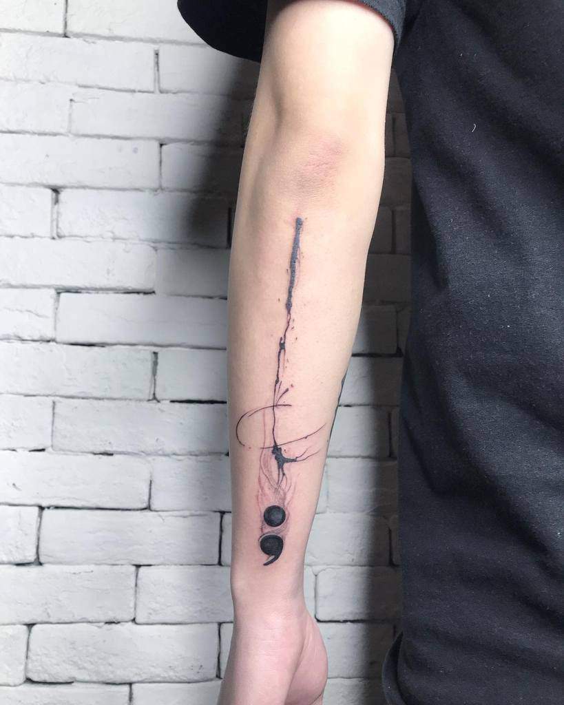 The tattoo features a flowing, ink-like design with a central semicolon, incorporating abstract lines and circles to create a sense of movement and depth on the forearm.