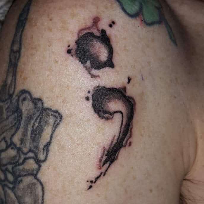 The tattoo features an artistic, ink-splattered semicolon design on the shoulder.