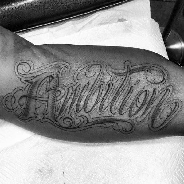 Arm tattoo flaunting "Ambition" in lavish cursive