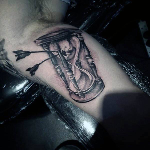 Tattoo of a cracked hourglass pierced by arrows, with a small skull inside, symbolizing mortality and the fleeting nature of time.