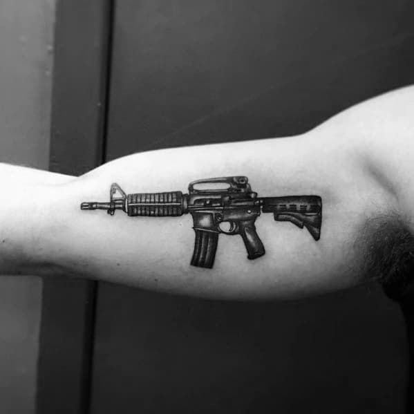 Black and grey AR-15 tattoo on the bicep, featuring a compact and detailed design, symbolizing strength, precision, and firearm appreciation.