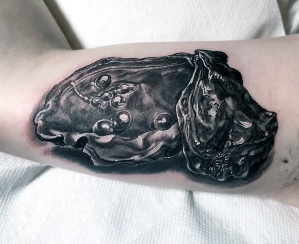 Hyper-realistic black and grey tattoo of an open oyster with multiple pearls, detailed with lifelike texture and shading on the inner arm.