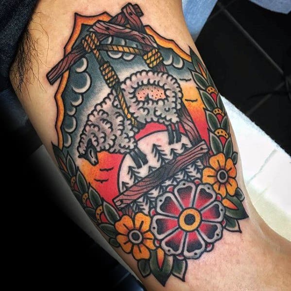 Colorful tattoo of a suspended sheep surrounded by flowers, leaves, and a sunset background