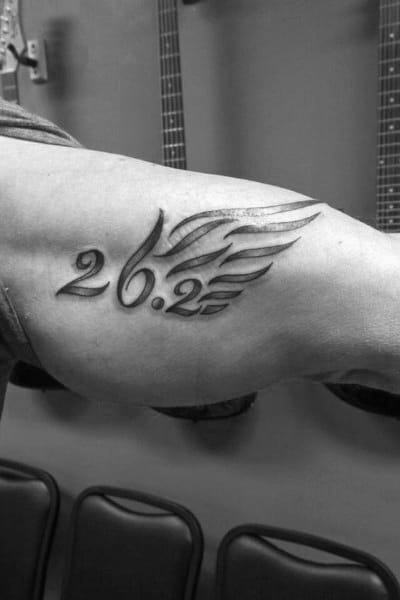 Bold 26.2 tattoo with stylized wings on the bicep, symbolizing strength, speed, and the freedom of completing a marathon.