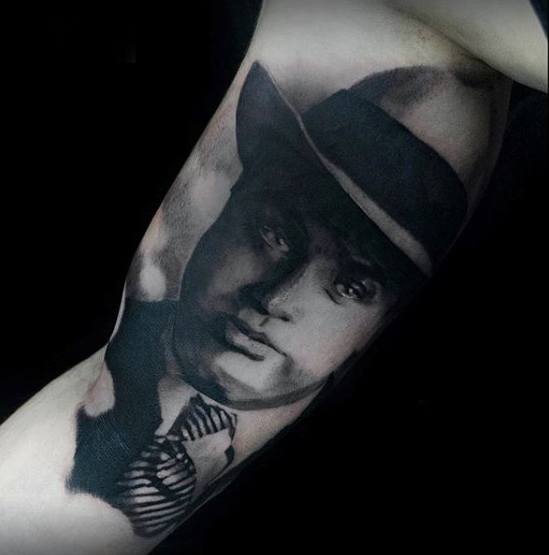 Al Capone tattoo featuring a black-and-white portrait of the gangster wearing his signature fedora, with a serious expression.