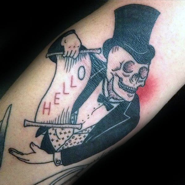 Tattoo of a skeleton in a tuxedo and top hat, holding a paper that says HELLO