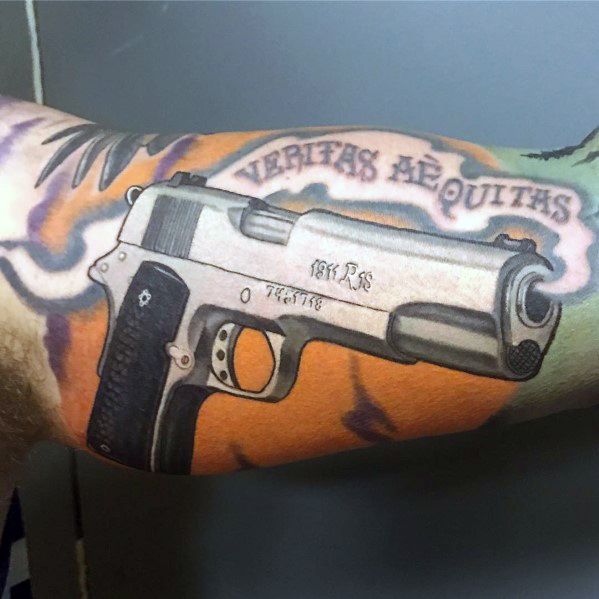 Realistic tattoo of a 1911 pistol on the forearm, featuring a two-tone design with "Veritas Aequitas" above, set against a colorful background.