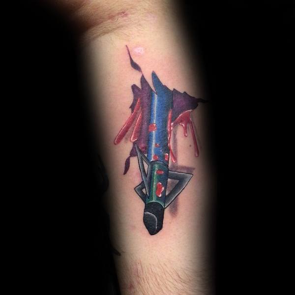 Color tattoo of a broadhead arrow piercing through the skin with vivid red blood details and torn flesh for a dramatic 3D effect.