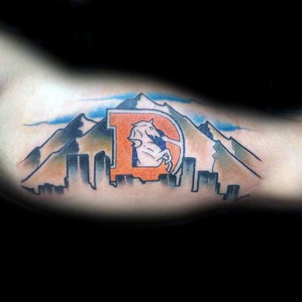 Denver skyline tattoo with mountains and an old-school Denver Broncos logo in orange and blue at the center of the design.