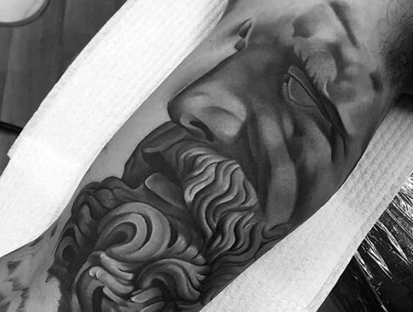 Inner arm tattoo for men featuring a hyper-realistic black and grey portrait of a bearded Greek or Roman statue.