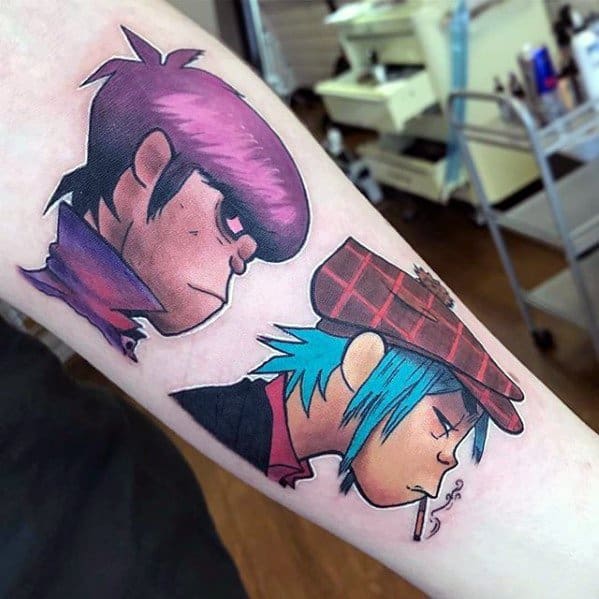 Vibrant forearm tattoo of Gorillaz members Murdoc and 2D in profile, featuring bold outlines, expressive faces, and rich color shading.