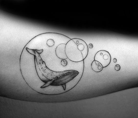 Black and grey tattoo of a whale swimming inside a bubble, with smaller bubbles surrounding it, creating a serene and whimsical underwater scene.