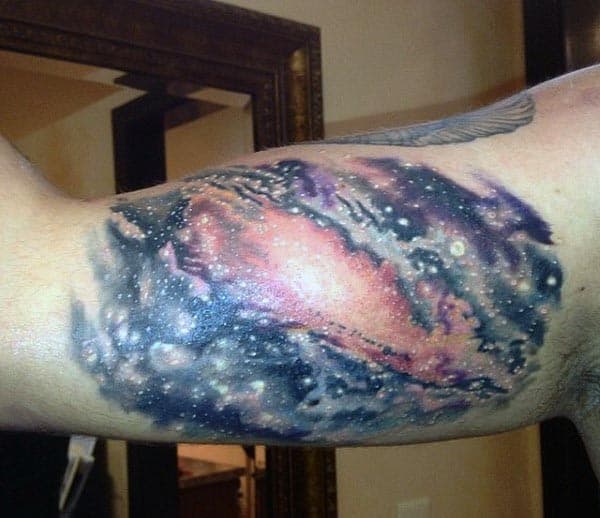 Colorful galaxy tattoo on the inner bicep, featuring a cosmic nebula with vivid red, blue, and purple hues and glowing stars