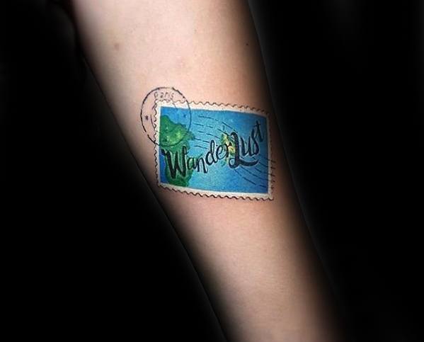 Vibrant tattoo of a postage stamp featuring the word 'Wanderlust' and a travel theme.
